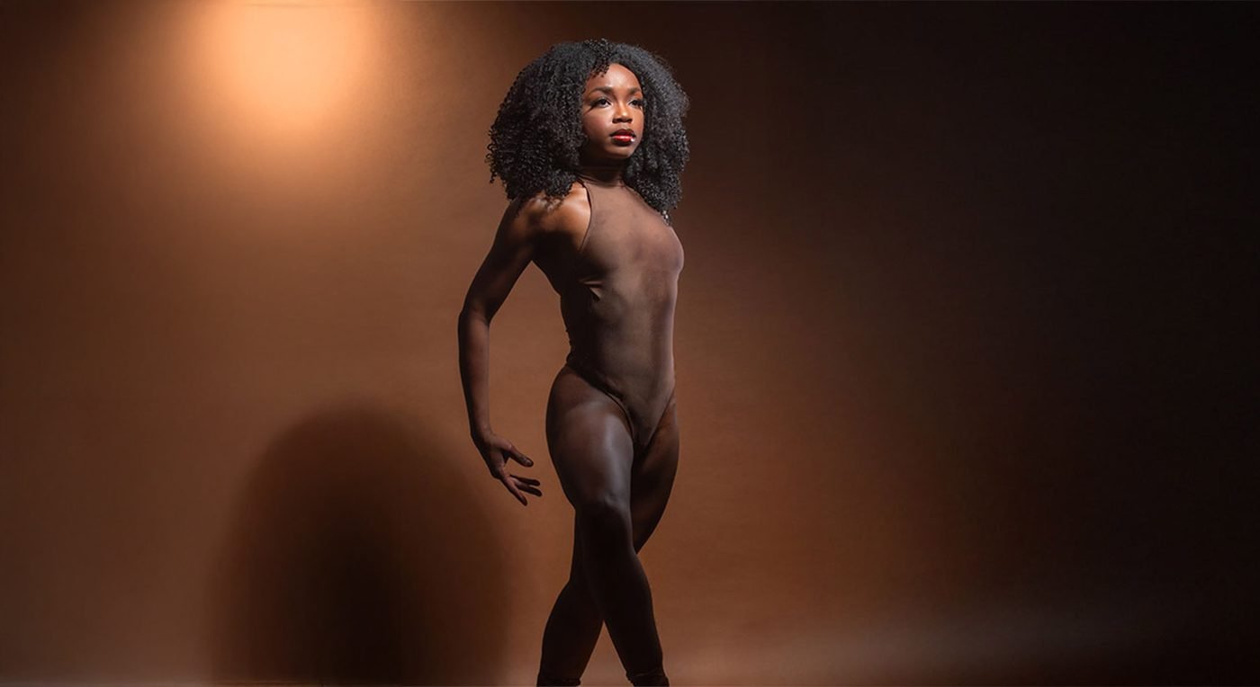 Dancer in a brown bodysuit posing under a warm spotlight