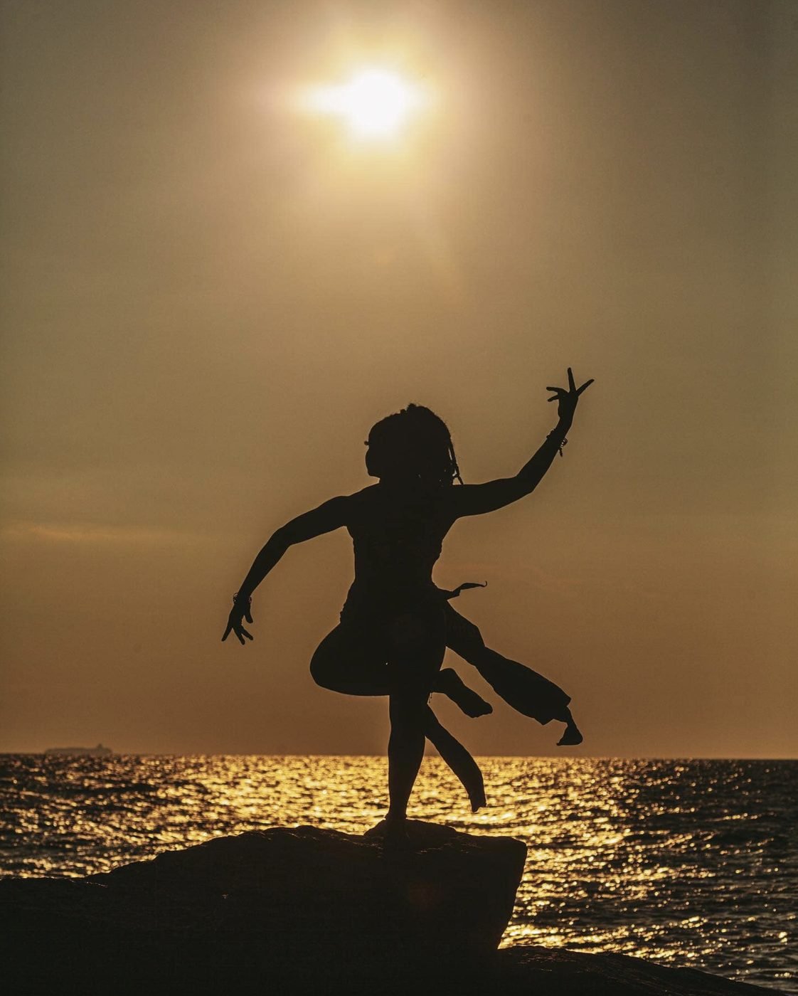 Silhouette of a dancer leaping on a rock at sunset over the sea